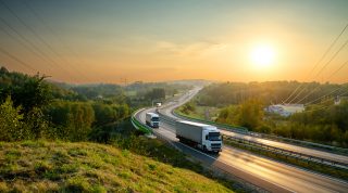 White trucks driving on the highway winding through forested landscape at sunset.