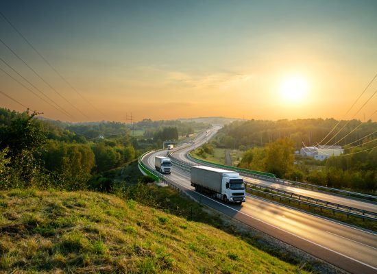 White trucks driving on the highway winding through forested landscape at sunset.